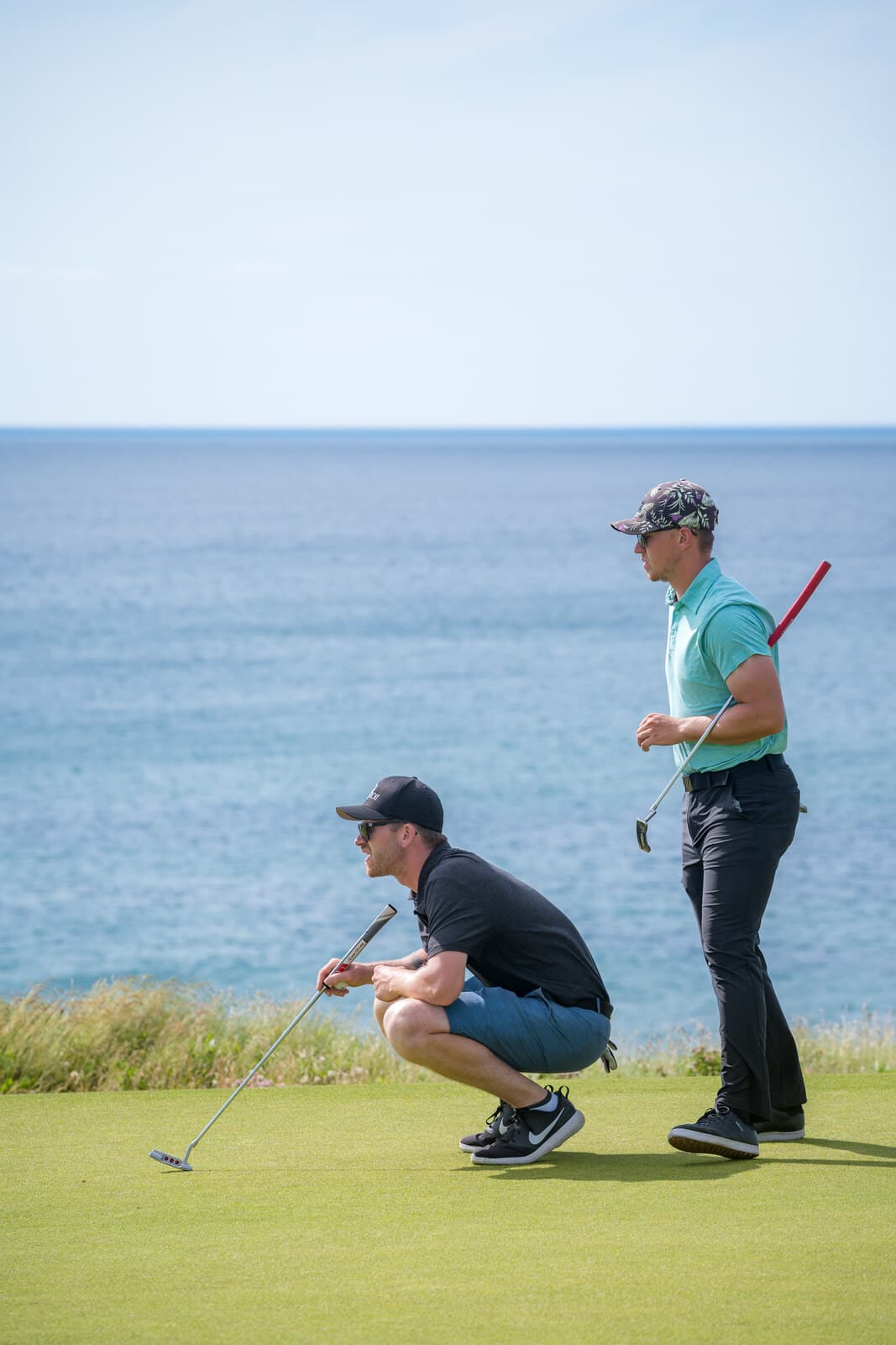 Golfers reading a putt on the green above the ocean, Cabot Cliffs