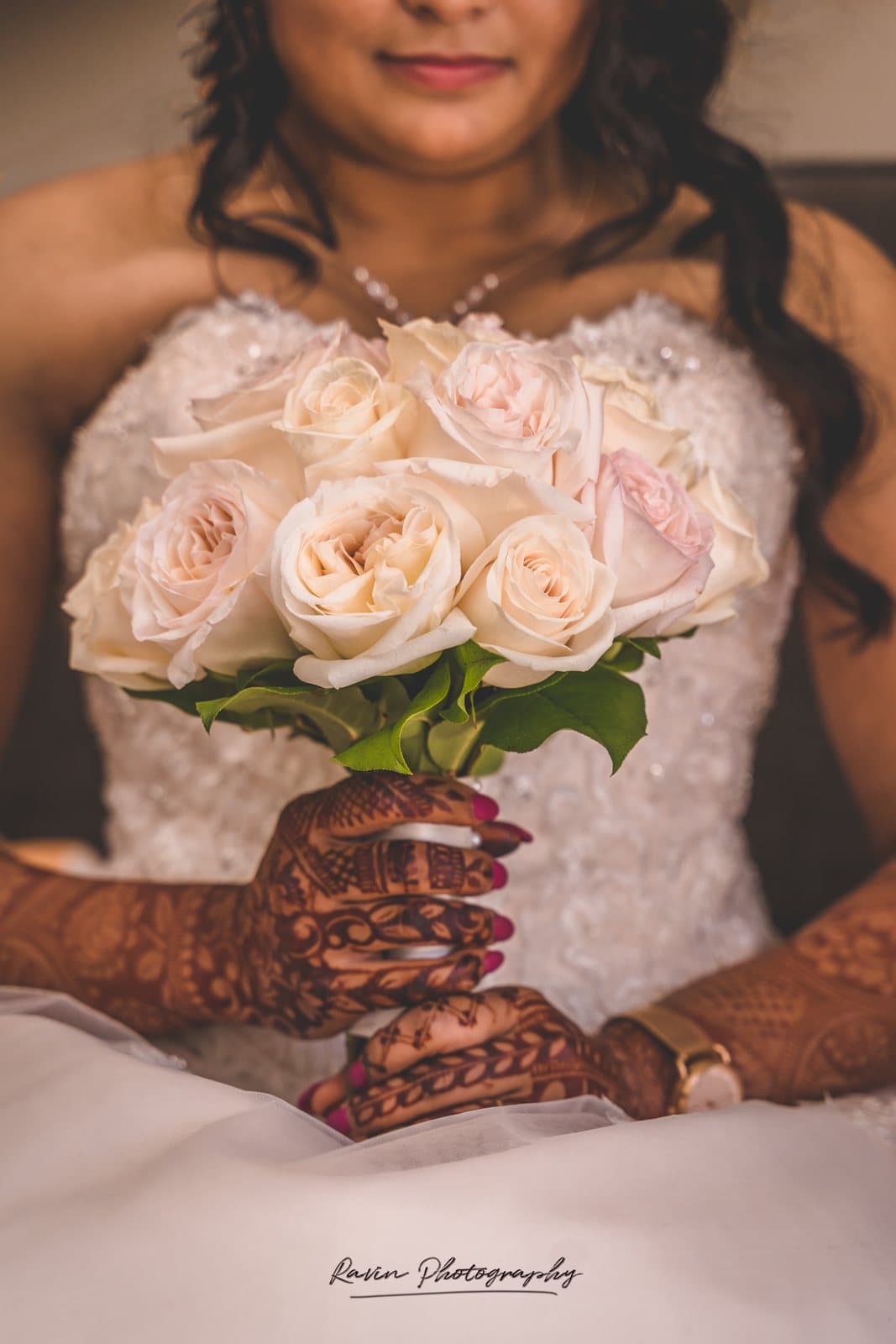 Bride holding a rose bouquet with henna-decorated hands, South Asian wedding