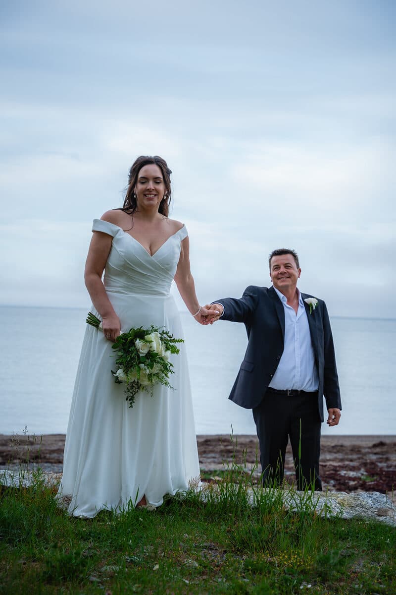 Bride and groom holding hands on a Nova Scotia beach, overcast sky