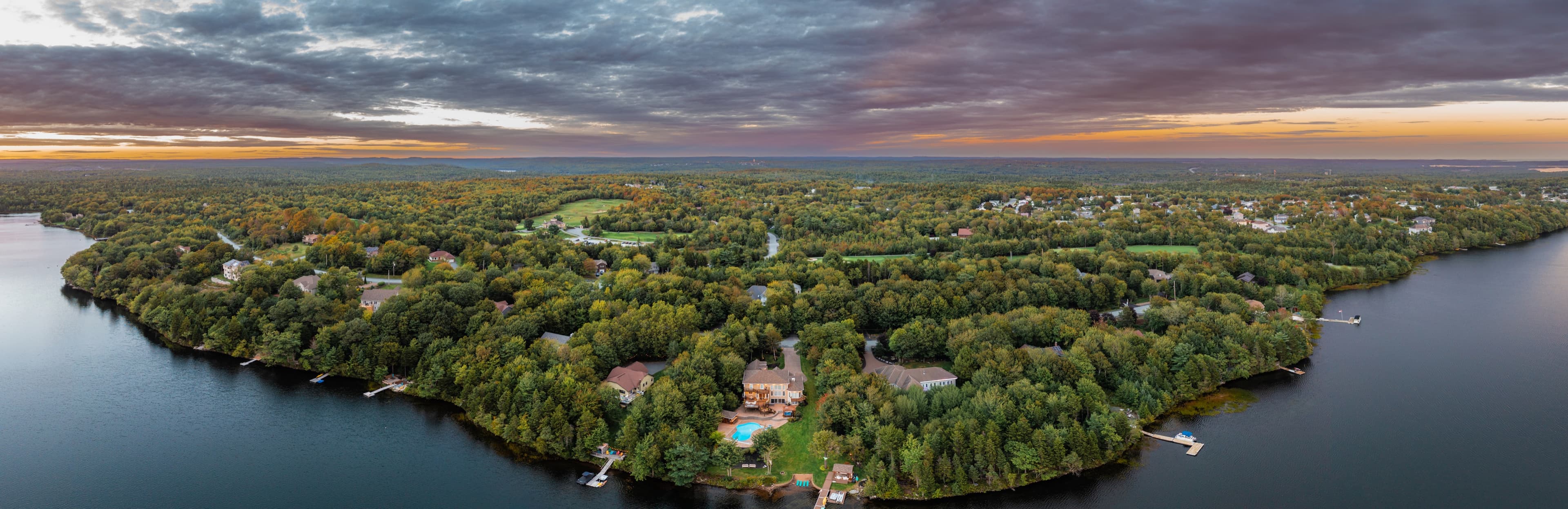 Aerial panorama at sunset of a wooded lakeside neighbourhood with docks along the shoreline