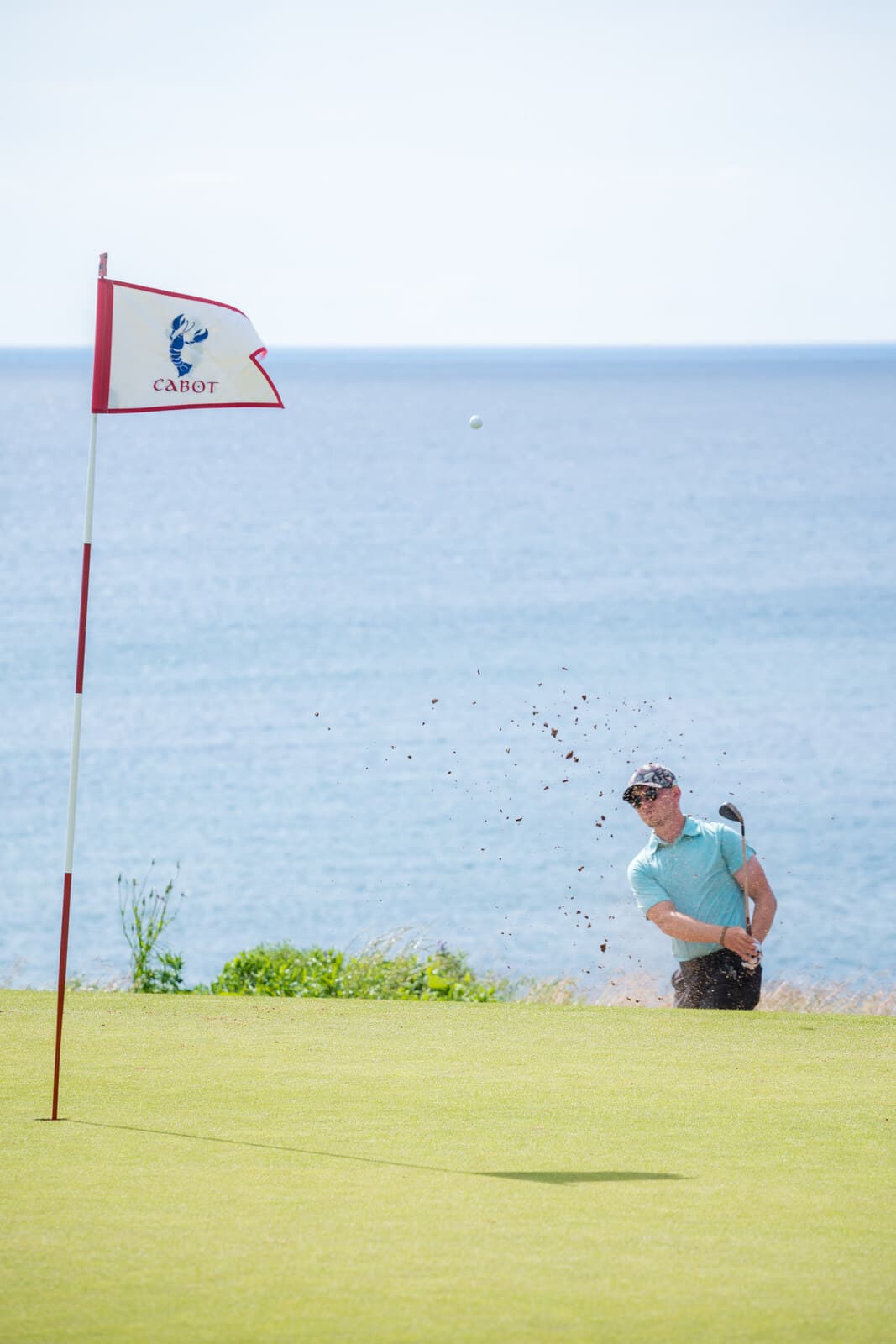 Golfer hitting from a bunker beside the ocean at Cabot Cliffs, Cape Breton